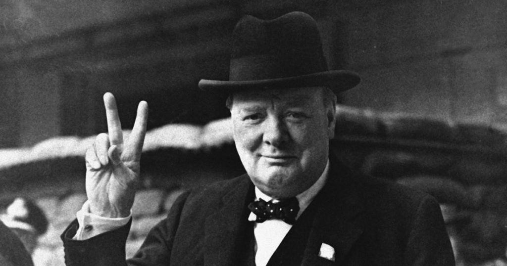 A man in a hat and bow tie is making a peace sign.