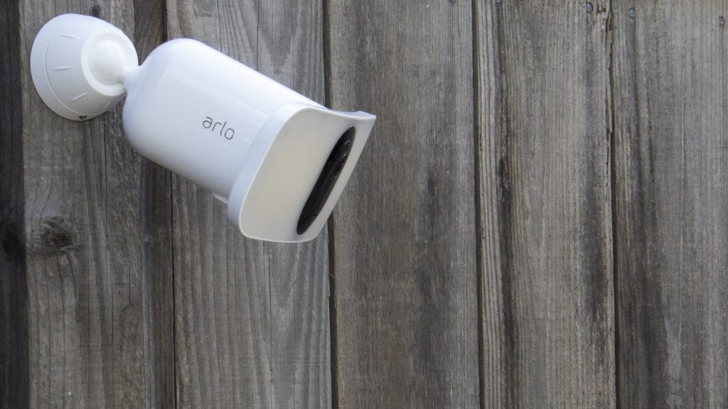 A white camera mounted on the side of a wooden fence.